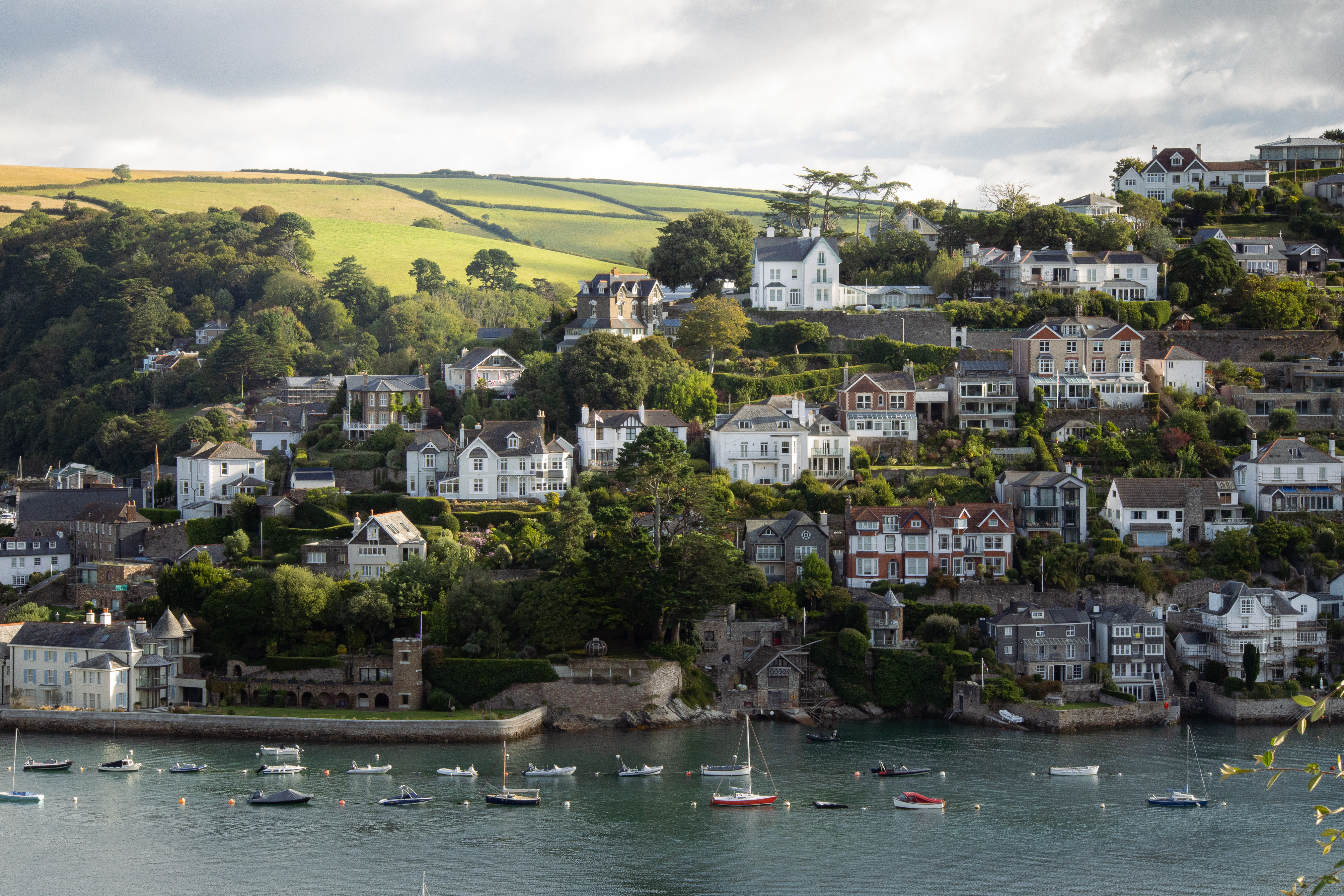 Salcombe-style harbour town of pastel houses set into a green Devon hillside above moored sailboats